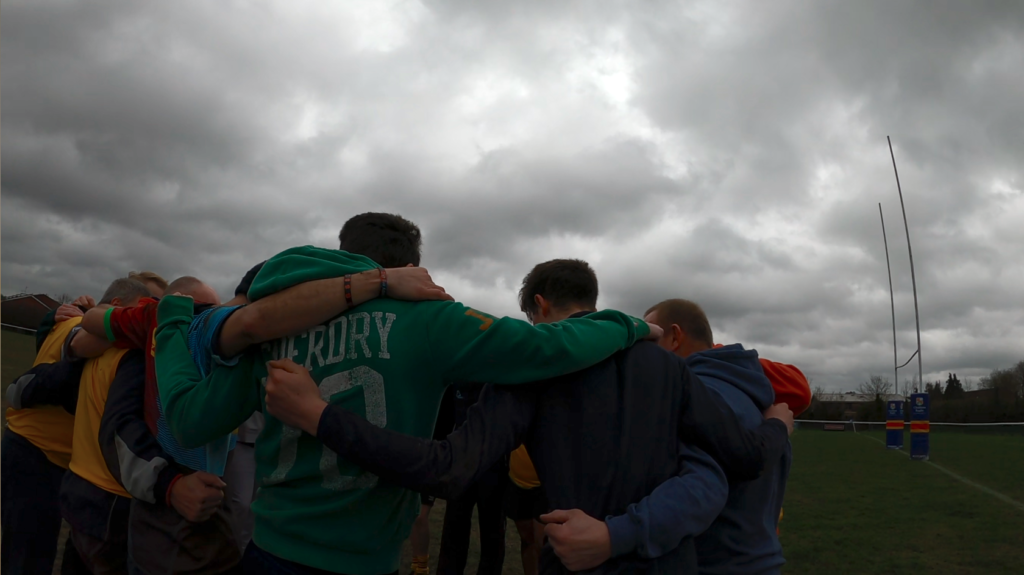 Photo of grey overcast sky over a rugby huddle depicting how weather can impact the meaning of a shot