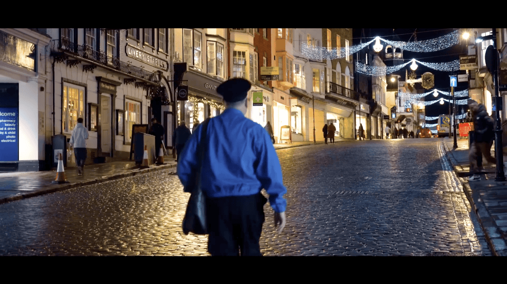 A post man walks up Guildford Highstreet at night lit up by Christmas lights
