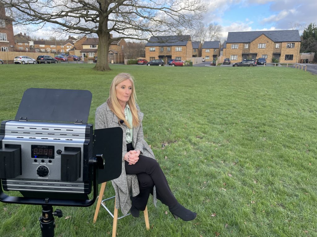 Presenter sat outside on a stool talking to camera with a light on them